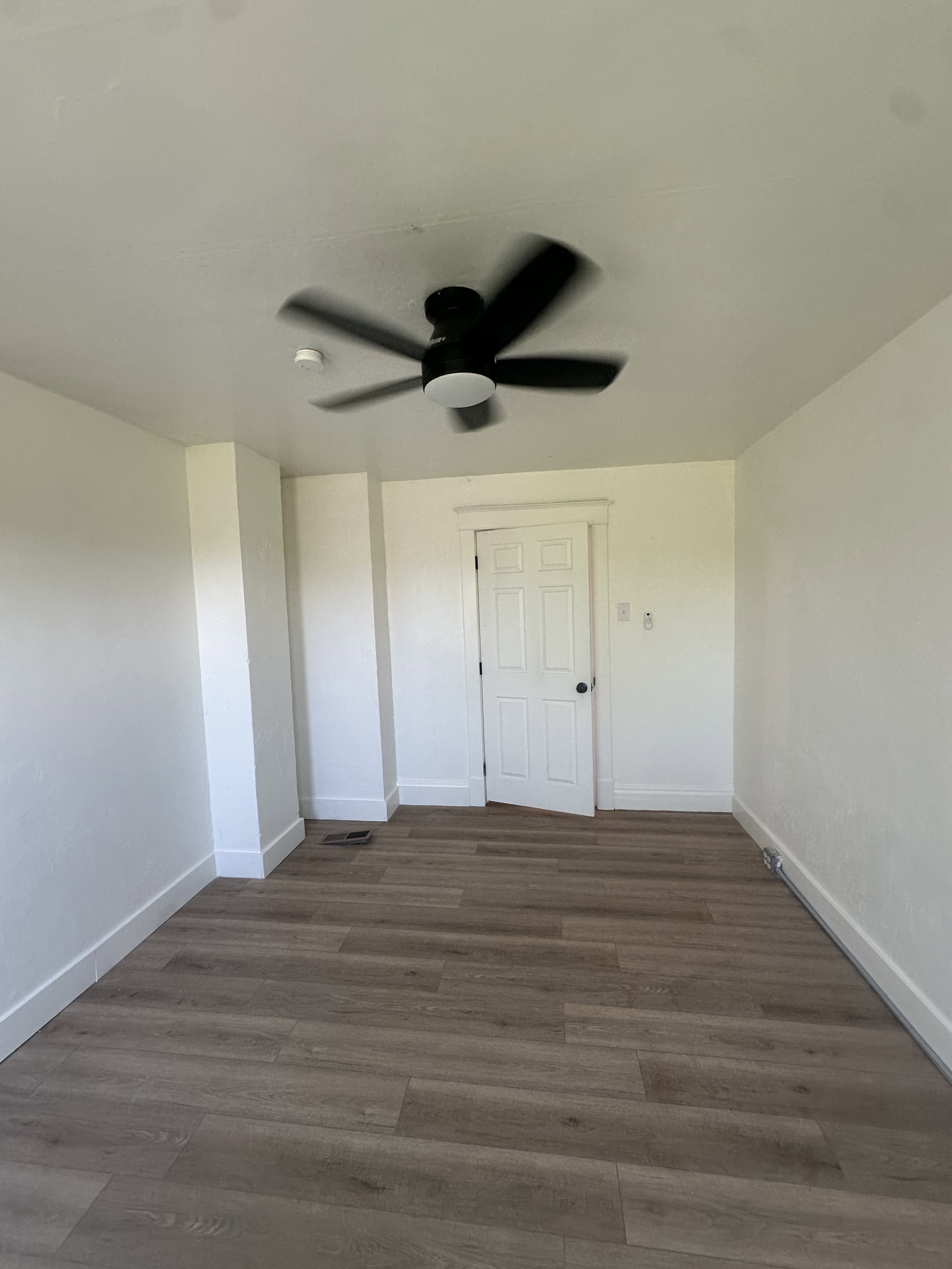 Room featuring wood-finish flooring, white baseboards, and a black ceiling fan with integrated lighting