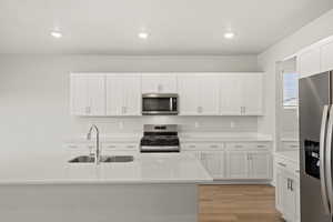 Kitchen featuring stainless steel appliances, light wood-style flooring, white cabinetry, light stone countertops, and recessed lighting