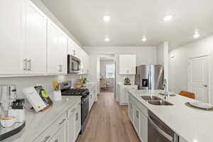 Kitchen featuring stainless steel appliances, light stone countertops, white cabinetry, light wood-style floors, and recessed lighting