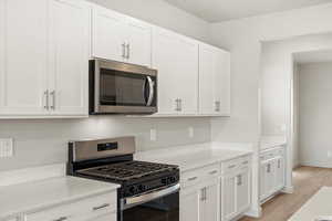 Kitchen featuring stainless steel appliances, white cabinetry, light stone counters, and light wood-type flooring