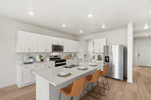 Kitchen with stainless steel appliances, white cabinets, light wood finished floors, a kitchen breakfast bar, and light stone countertops