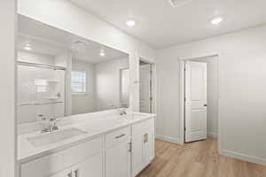 Full bathroom with double vanity, light wood finished floors, a shower stall, and recessed lighting