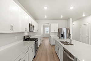 Kitchen with stainless steel appliances, light stone countertops, light wood-type flooring, white cabinets, and recessed lighting