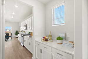 Kitchen featuring white cabinetry, stainless steel appliances, light wood-style flooring, recessed lighting, and light stone counters