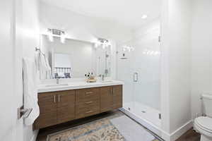Full bath with double vanity, a shower stall, and dark wood-type flooring