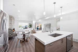 Kitchen featuring stainless steel appliances, a stone fireplace, dark wood finish cabinets, light stone counters, and open floor plan