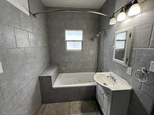 Full bathroom with tile walls, vanity, a combined bath / shower with jetted tub, and dark tile patterned flooring