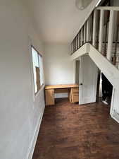 Unfurnished office with built in desk, dark wood finished floors, and a textured wall