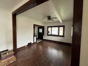 Empty room with dark wood-type flooring, beam ceiling, and a ceiling fan
