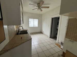 Kitchen with tile countertops, light tile patterned floors, white cabinets, a ceiling fan, and crown molding