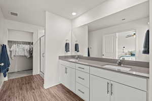 Ensuite bathroom featuring double vanity, a spacious closet, dark wood-type flooring, a stall shower, and ceiling fan