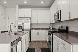Kitchen featuring stainless steel appliances, white cabinetry, a kitchen island with sink, light wood-type flooring, and recessed lighting