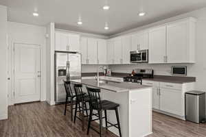 Kitchen featuring a breakfast bar area, a kitchen island with sink, white cabinetry, stainless steel appliances, and dark wood-type flooring