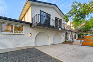 View of front facade with a balcony, concrete driveway, stucco siding, an attached garage, and brick siding