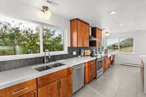 Kitchen featuring wood finish cabinets, light stone counters, stainless steel appliances, light tile patterned flooring, and a baseboard radiator