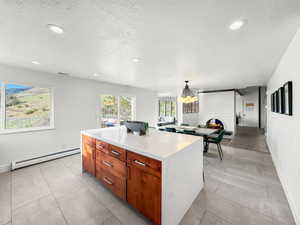 Kitchen featuring wood finish cabinets, a center island, a baseboard radiator, light stone countertops, and a textured ceiling