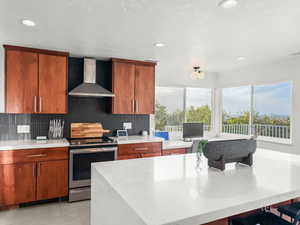 Kitchen with wood finish cabinetry, stainless steel range with electric stovetop, recessed lighting, light stone counters, and backsplash