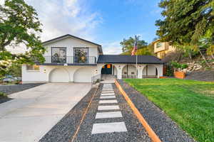 Tri-level home with driveway, an attached garage, a balcony, a front lawn, and brick siding