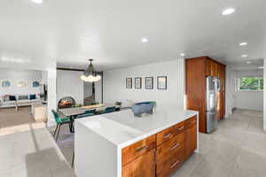 Kitchen featuring wood finish cabinetry, a kitchen island, stainless steel fridge with ice dispenser, light stone counters, and open floor plan
