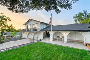 Rear view of house featuring a shingled roof, a garage, a yard, concrete driveway, and a balcony