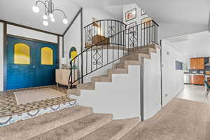 Foyer entrance featuring a chandelier, vaulted ceiling, light colored carpet, french doors, and light tile patterned floors