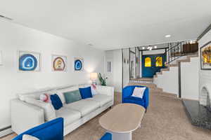 Carpeted living room featuring stairway and a baseboard radiator
