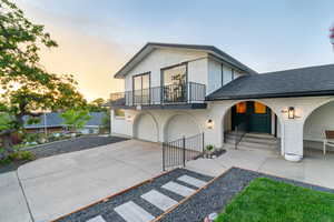 View of front facade with a balcony, concrete driveway, stucco siding, a shingled roof, and an attached garage