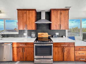 Kitchen with wood finish cabinetry, stainless steel appliances, a textured ceiling, decorative backsplash, and light stone countertops