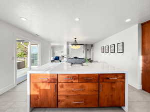 Kitchen with wood finish cabinetry, a kitchen island, light stone countertops, and a textured ceiling