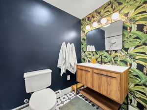 Half bathroom with vanity, an accent wall, baseboard heating, and wallpapered walls