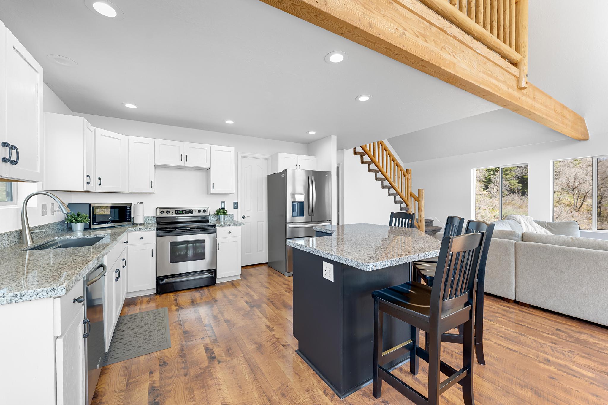 Open-concept kitchen featuring white cabinetry, stainless steel appliances, granite countertops, and wood-finish flooring