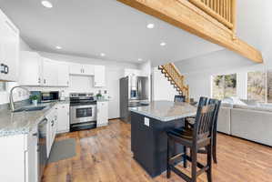 Open-concept kitchen featuring white cabinetry, stainless steel appliances, granite countertops, and wood-finish flooring