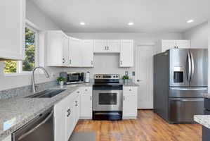 Kitchen featuring white cabinetry, light-toned granite countertops, and wood-finish flooring
