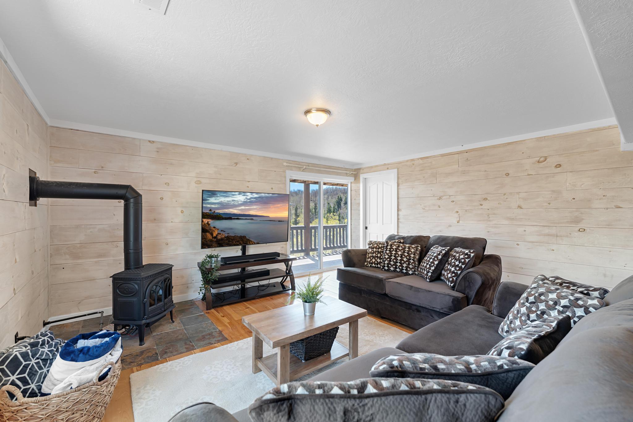 Living area featuring a cast iron wood-burning stove on a stone tile hearth, wood-finish flooring, plank wall finishes, and a sliding glass door opening to a balcony with mountain scenery