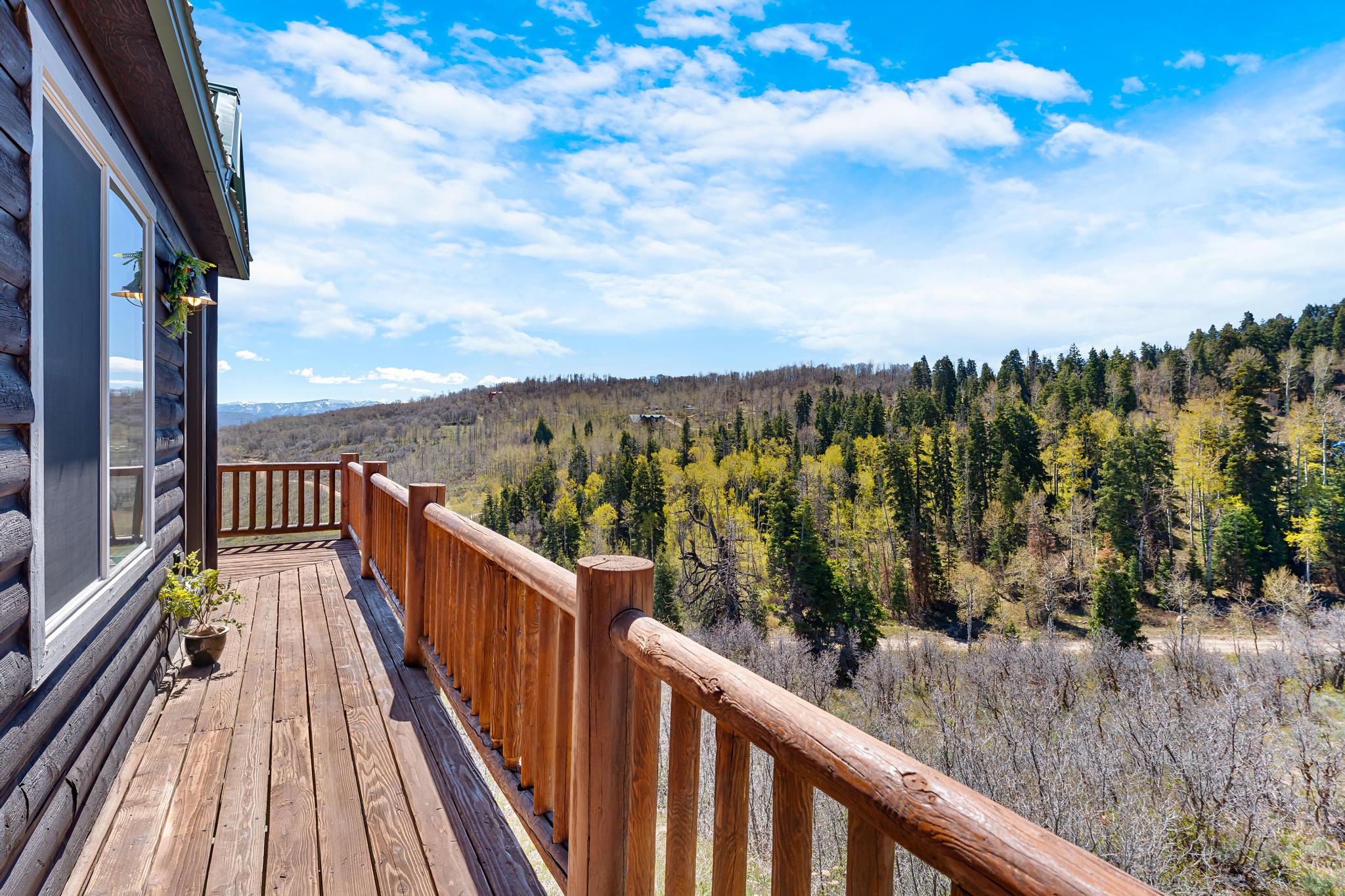 Expansive wood-plank deck with natural wood railings, offering elevated perspectives of the surrounding forest and distant mountains