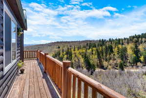Expansive wood-plank deck with natural wood railings, offering elevated perspectives of the surrounding forest and distant mountains