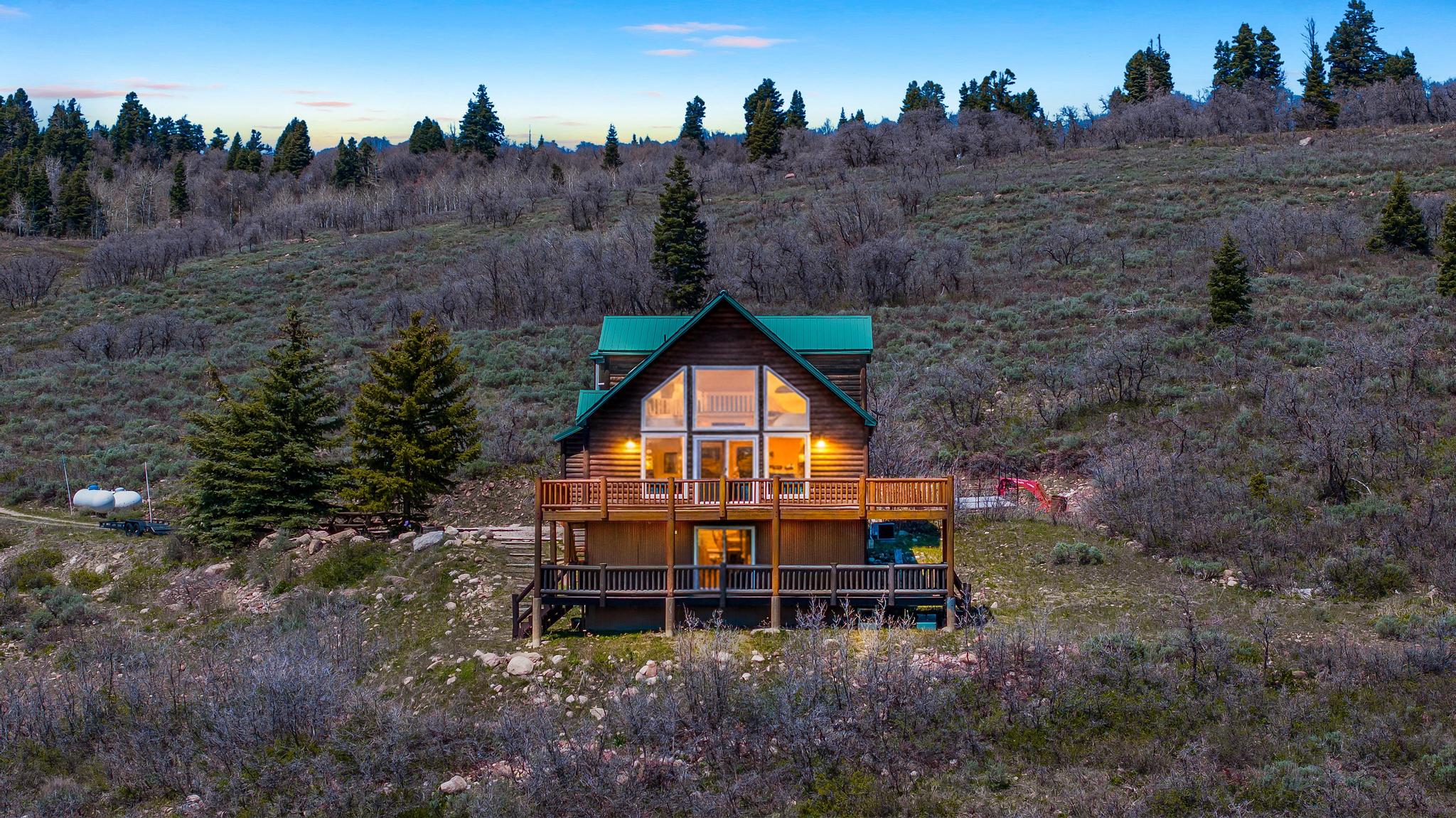 Log cabin exterior featuring a steep-pitched metal roof, two levels of outdoor decking, and a prominent gable with large windows