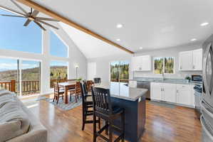 Open-concept living space featuring vaulted ceilings with exposed wood beams, a ceiling fan, and wood-finish flooring