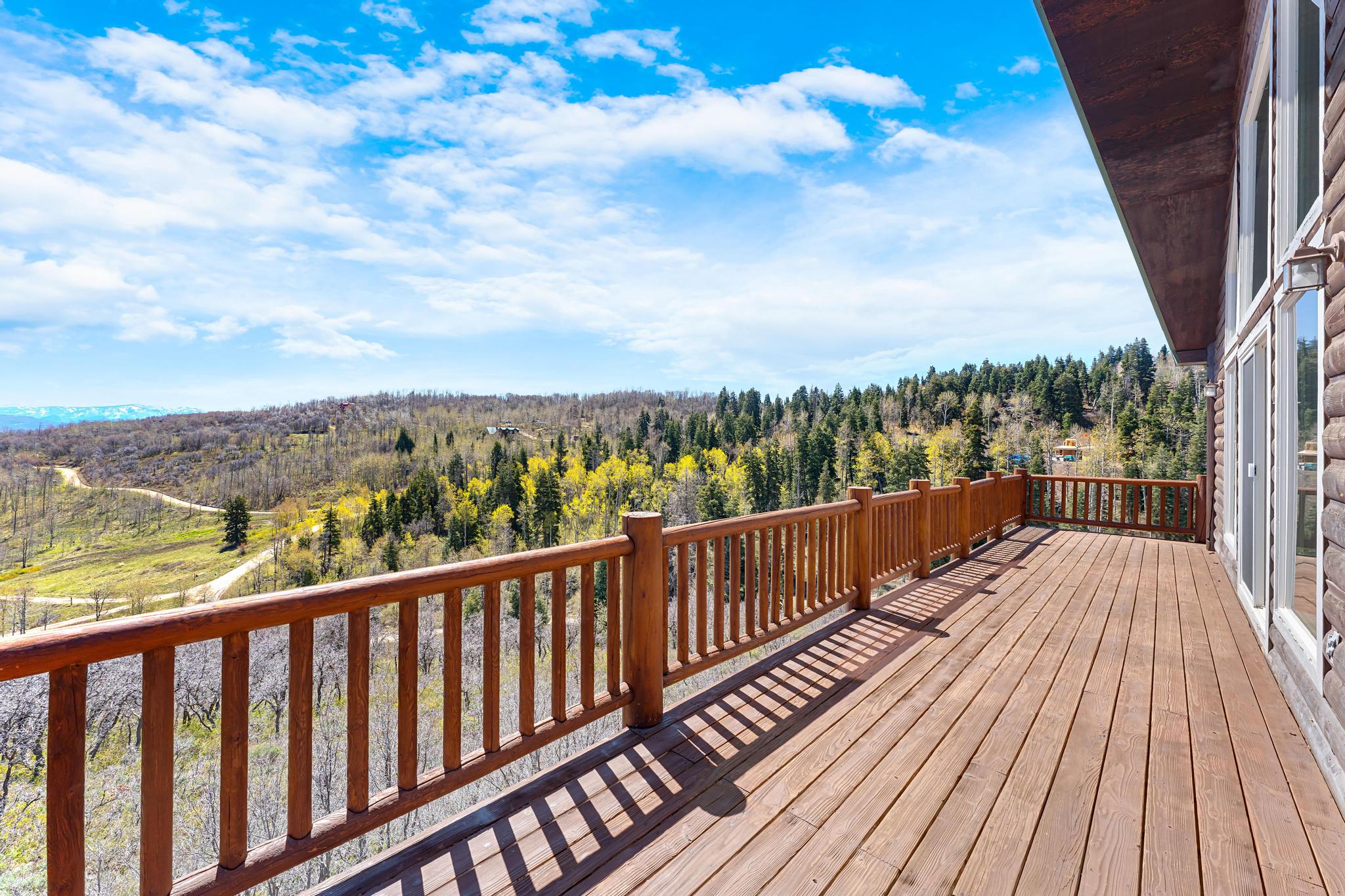 Expansive wood deck with a matching wood railing, offering sweeping mountain and forest scenery