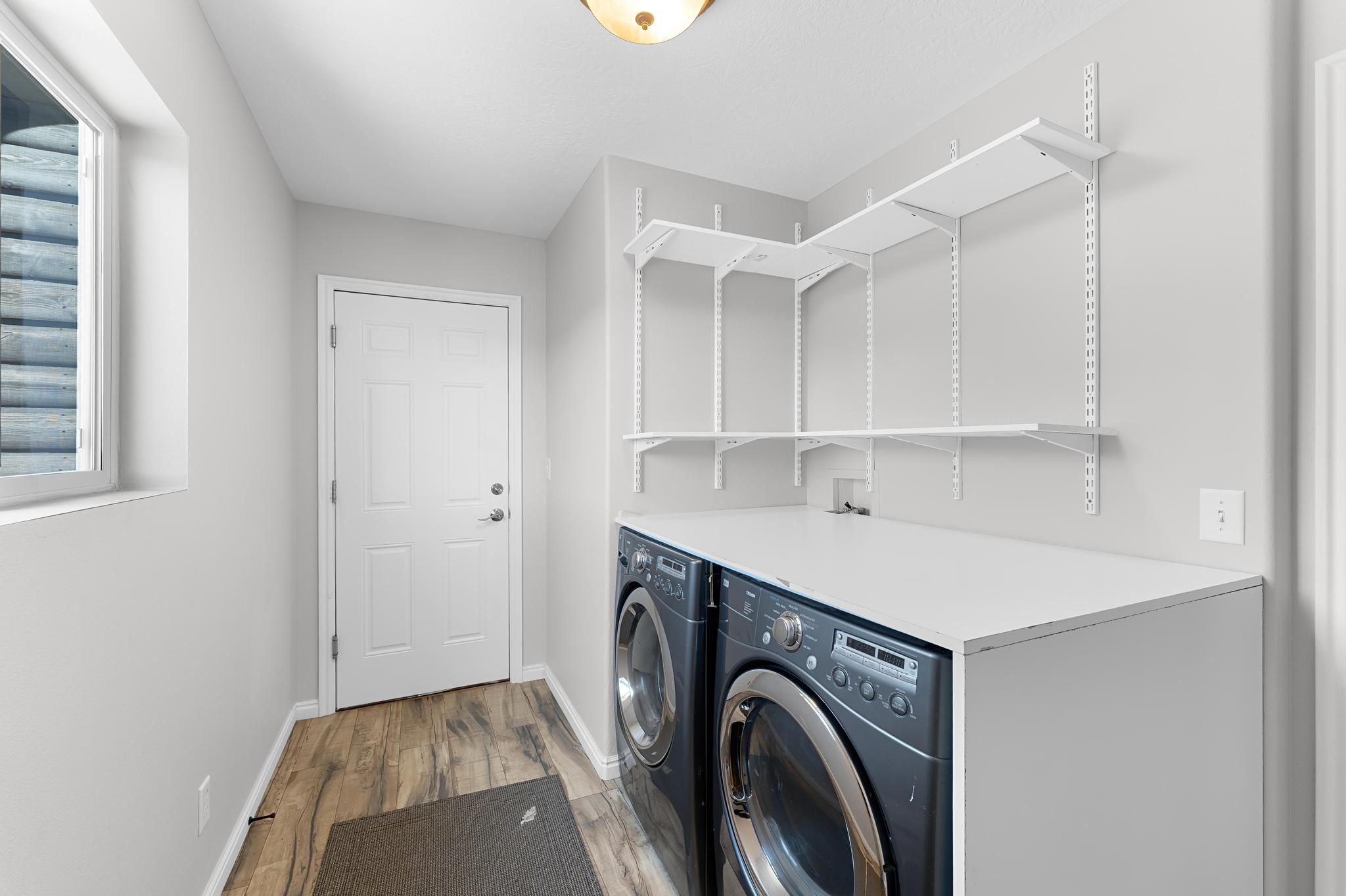 Dedicated laundry space featuring side-by-side appliances, a white laminate countertop, and wood-finish flooring