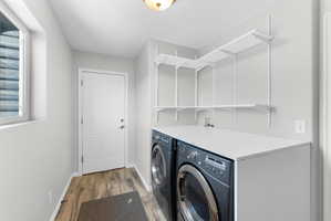 Dedicated laundry space featuring side-by-side appliances, a white laminate countertop, and wood-finish flooring