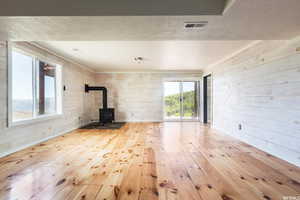 Unfurnished living room featuring light wood finished floors, a wood stove, a textured ceiling, and wooden walls