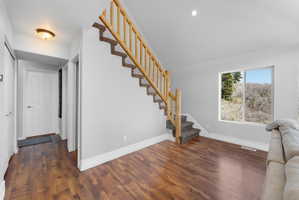 Interior space featuring wood-finish flooring, a carpeted staircase with wood railing, a hallway with a paneled door, and a large window showcasing natural scenery
