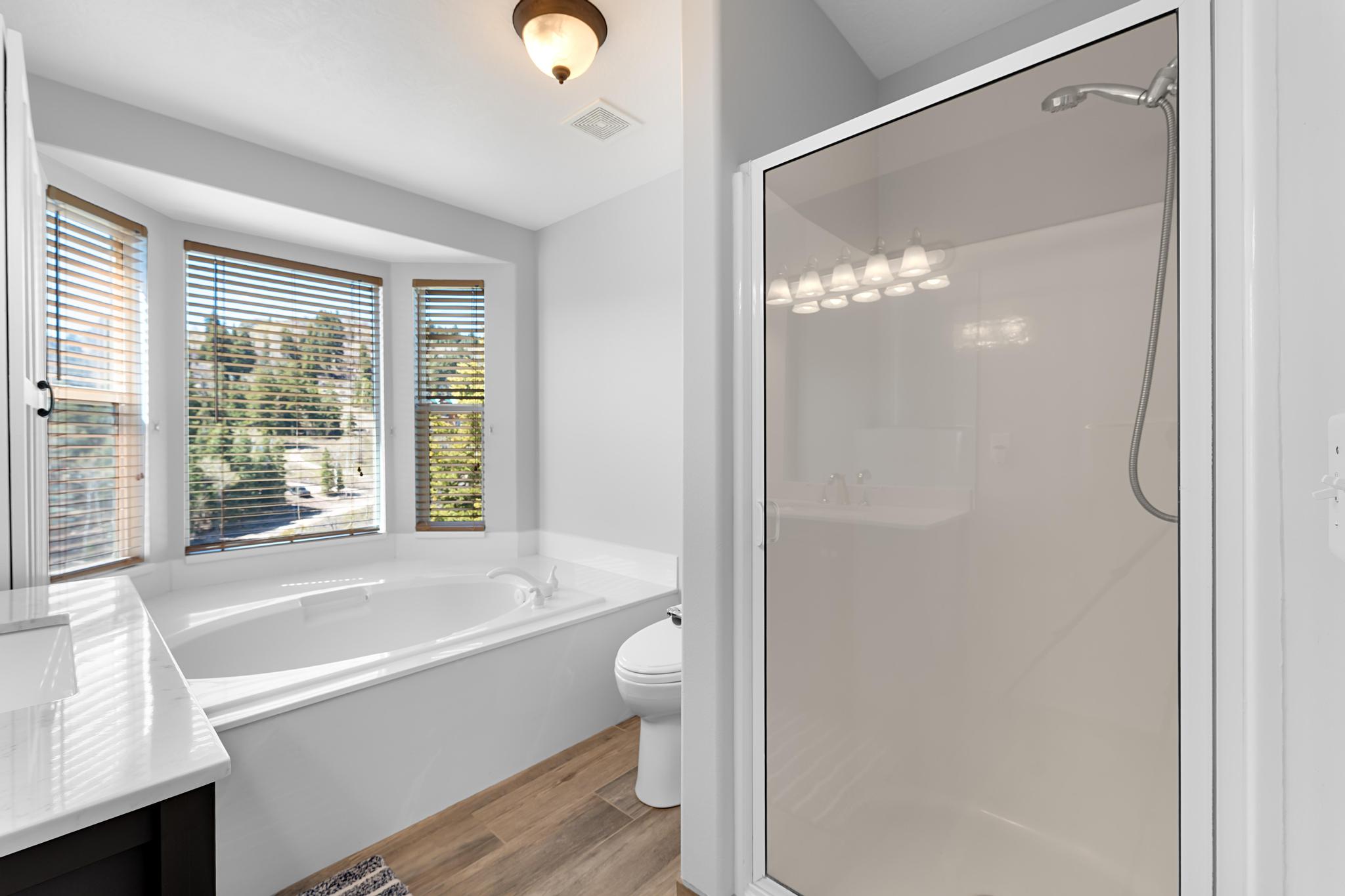 Soaking tub with a bay window, separate glass-enclosed shower, wood-finish flooring, and a vanity with a white countertop