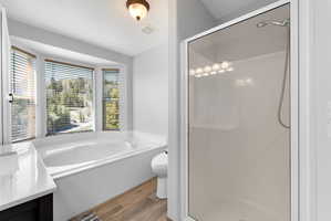 Soaking tub with a bay window, separate glass-enclosed shower, wood-finish flooring, and a vanity with a white countertop