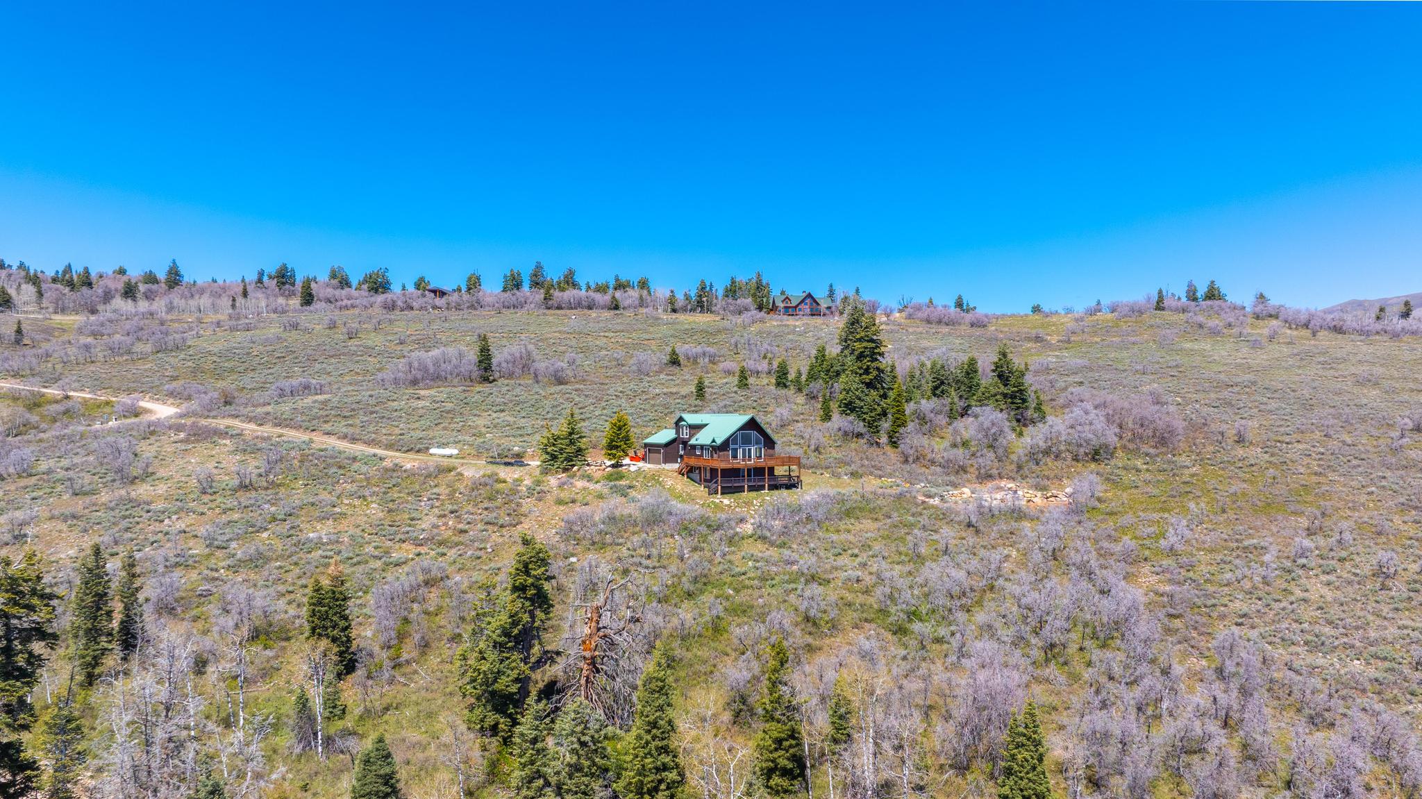Spacious hillside property featuring a multi-level residence with a wood-finish exterior, a dark green roof, and a large wraparound deck