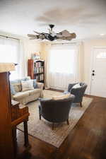 Living room featuring dark wood-style floors, healthy amount of natural light, and a ceiling fan