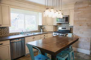 Kitchen with decorative backsplash, dark countertops, stainless steel appliances, cream cabinets, and hanging light fixtures