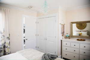 Bedroom featuring a closet, ornamental molding, stacked washing machine and dryer, and a chandelier