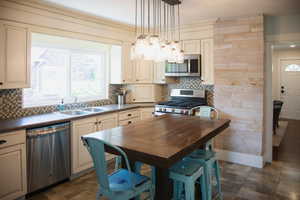 Kitchen with dark countertops, stainless steel appliances, backsplash, and cream cabinetry